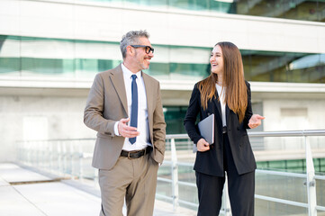 A mature businessman with grey hair and young colleague both smile as they engage in a professional...