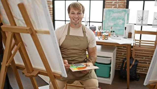 Portrait of a focused man painting in a sunlit art studio, showcasing creativity and concentration.