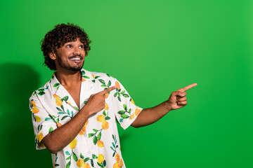 Photo of funky dreamy arabian man wear print shirt winking looking showing two fingers empty space isolated green color background