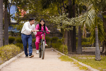 Indian Latin Father helping Daughter With cycling in Outdoor Garden