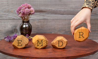 Letters EMDR written on irregular wooden blocks. A woman's hand adds the last block, Eye Movement...