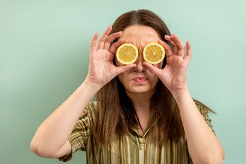 Portrait of a young woman holding lemon slices over her eyes. 