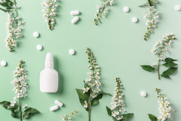 Seasonal spring allergies, fresh spring blooming branches tree and mock up white nasal spray bottle, pills on green background, top view, minimal flat lay Seasonal allergy treatment concept.