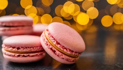 Fotobehang pink macarons on a black surface in focus against blurred yellow and orange lights in the background © Marsha