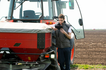 Young farm worker next to tractor using digital tablet