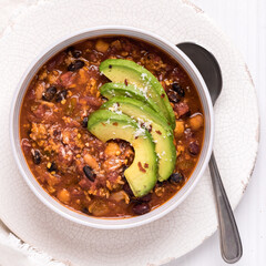 A bowl full of healthy black bean chili topped with avocado, ready for eating.