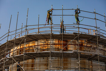 Fototapeta premium Construction workers installing scaffolding storage tank Oil​ refinery​ and​ plant and tower column