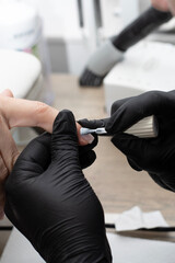 Beauty concept. A manicurist in black latex gloves makes a hygienic manicure and paints the client's nails with gel polish in a beauty salon. Close-up.