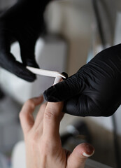 Beauty concept. A manicurist in black latex gloves makes a hygienic manicure, paints the client's nails with gel polish and files them with a nail file in a beauty salon.