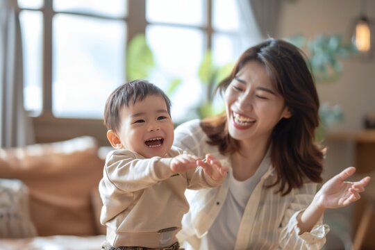 Happy asian american mother with her son dancing at home together, spending leisure time in living room, smiling young mom and adorable boy child moving to favorite music, family engaged in funny acti