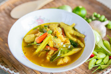 Thai green curry with chciken and vegetables in white bowl on wooden table.