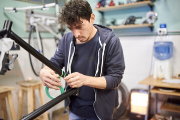 Man preparing a bicycle frame with masking tape to paint it in his workshop.