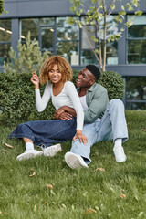 excited african american couple hugging and sitting together on green grass, happiness