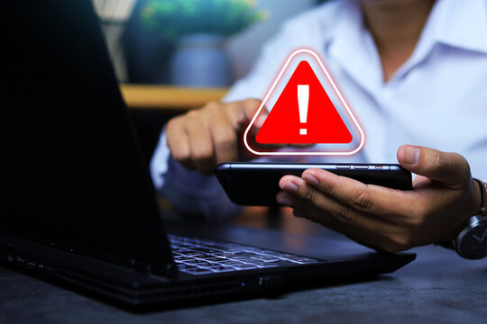 Businessman found alert sign on smartphone screen by system warning about information security or hacker may use login account to commit cyber crimes. Cyber security concept
