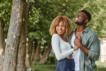 Fototapeta premium cheerful african american couple holding hands and hugging each other outdoors, woman in braces