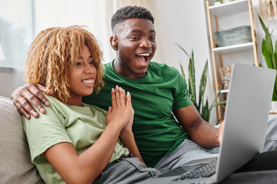 excited african american man in hearing aid device watching movie on laptop with girlfriend