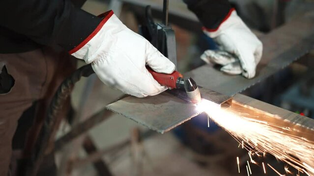 Shimmering flames and sparks in metal workshop, industrial worker in protective gloves using cutting torch of oxygen and acetylene mixture to heat metal surface and divide with pressure. Metal