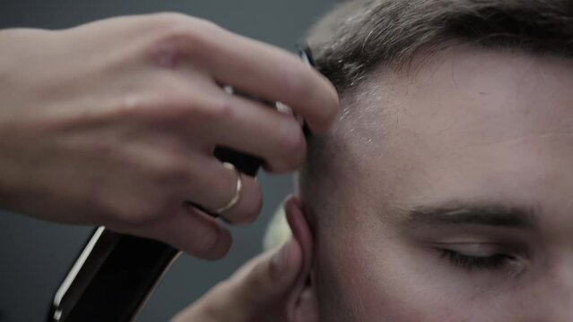 A handsome male hairdresser cuts a caucasian male client with a hair clipper and styles his hair with a comb. Professional haircut in a barbershop. Stylish and fashionable haircut. Slow motion