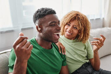 excited african american man in hearing aid device sitting near happy girlfriend in braces