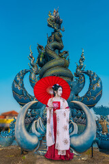 Asian female tourist in Chinese national costume stands admiring a blue statue in a temple in Chiang Rai Province, Thailand. - 737254588