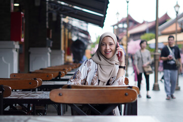 Indonesian Woman wearing Hijab Engaging in Digital Conversations at Cafe Bench