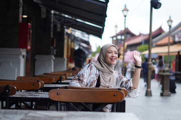 Indonesian Hijabi Woman Waving at a Distance or Calling the Cafe Attendant or Calling her Friend