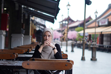 Serene Contemplation concept. Indonesian Hijabi Woman Lost in Thought at Cafe Bench