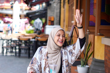 Indonesian Hijabi Woman Waving at a Distance or Calling the Cafe Attendant or Calling her Friend