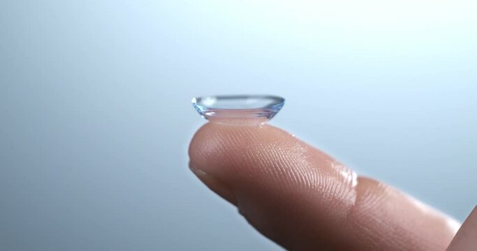 Super slow motion of drop of liquid solution for clean and disinfect is falling on contact eye ophthalmology optometry care optical lens kept on finger isolated on soft background at 1000 fps.