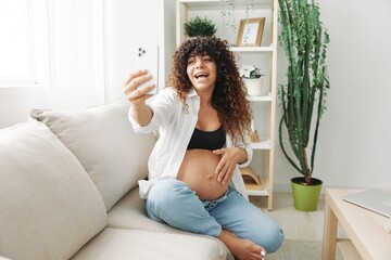 Pregnant woman blogger sits on the couch at home and takes pictures of herself on the phone, selfie and video call, consultation with the doctor online, pregnancy management