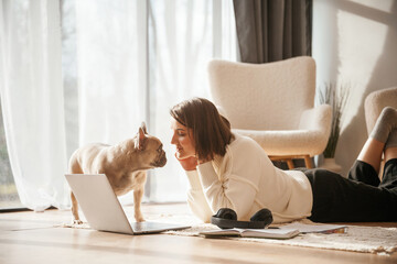 Wooden floor. With laptop. Young woman is with her pug dog at home