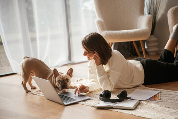 Animal is curious about laptop. Young woman is with her pug dog at home