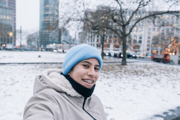 Teenager in light blue cap taking a selfie in the snowy streets of Berlin