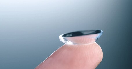 Super slow motion of drop of liquid solution for clean and disinfect is falling on contact eye ophthalmology optometry care optical lens kept on finger isolated on soft background at 1000 fps.