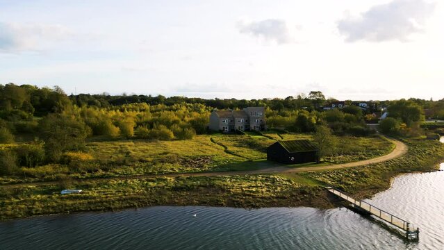 Herbstliche Stimmung in l&auml;ndlicher Gegend mit gro&szlig;em Landhaus, Nebengeb&auml;uden und einem privaten Anleger am See. Drohnenaufnahme. Fisken&aelig;svej, Gr&aring;sten, D&auml;nemark