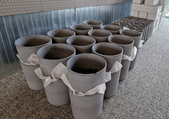 gray concrete flower pots, lined up in a warehouse in rows for sale. plastic white tubs of bricks...