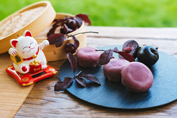 Wooden lucky cat figurine beside a plate of food on a table. Mochi asian dessert