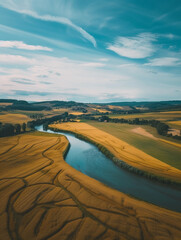 Drone perspective over an agricultural landscape golden wheat fields next to a river with small farmhouses dotting the horizon