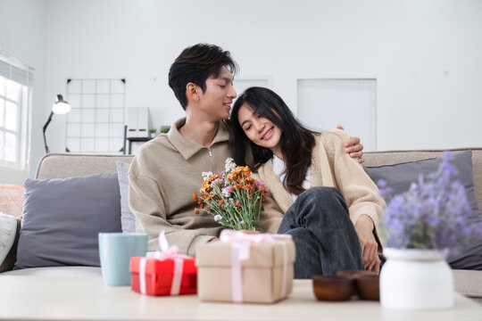 A young Asian couple gives flowers to each other on their anniversary and sits happily together in the living room.