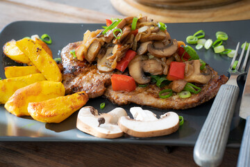 Jägerschnitzel - gebratener Schweinsschopf mit Champignons und Zwiebel, Kartoffelspalten als Beilage