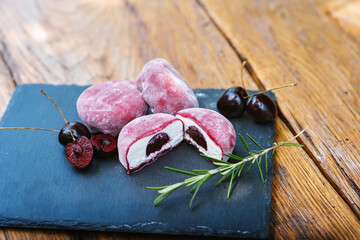 A slate rectangle cutting board with ice cream and cherries on a wooden table. Mochi asian dessert