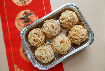 close up of Chinese New Year deep fried taro ball nests snacks in a tin foil container. There is a red paper called Fai Chun with Chinese word written 