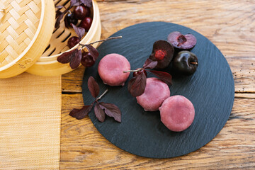 A bamboo steamer filled with cherries and plums rests on a wooden table. Mochi asian dessert