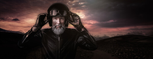 Portrait d'un motard biker homme avec un casque noir et une veste en cuir et des lunettes de protection et une barbe grise vintage - obrazy, fototapety, plakaty