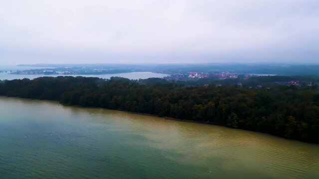 Nebeliger Morgen &uuml;ber einer bewaldeten Bucht und der stillen Wasserlandschaft mit Stadt in der Ferne. Drohnenaufnahme. Fisken&aelig;svej, Graasten, D&auml;nemark