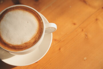 Coffee in white cup on wooden table, with spoon.