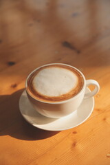 Coffee in white cup on wooden table, with spoon.