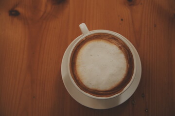 Coffee in white cup on wooden table, with spoon.