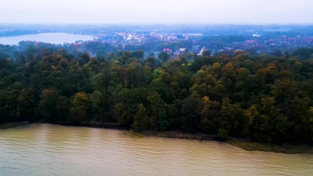 Herbstliche Flusslandschaft mit dichtem Wald und einer Kleinstadt im Hintergrund bei Morgend&auml;mmerung. Drohnenaufnahme Parallelfahrt. Fisken&aelig;svej, Graasten, D&auml;nemark