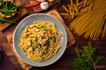 Stir fried spicy spaghetti with minced chicken breast and basil leaves in white plate,Spicy pasta Pad Kra Pao.Healthy Thai fusion food.Top view - obrazy, fototapety, plakaty
